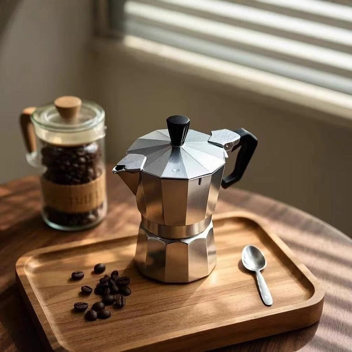 Moka pot i aluminium på träbricka med kaffebönor